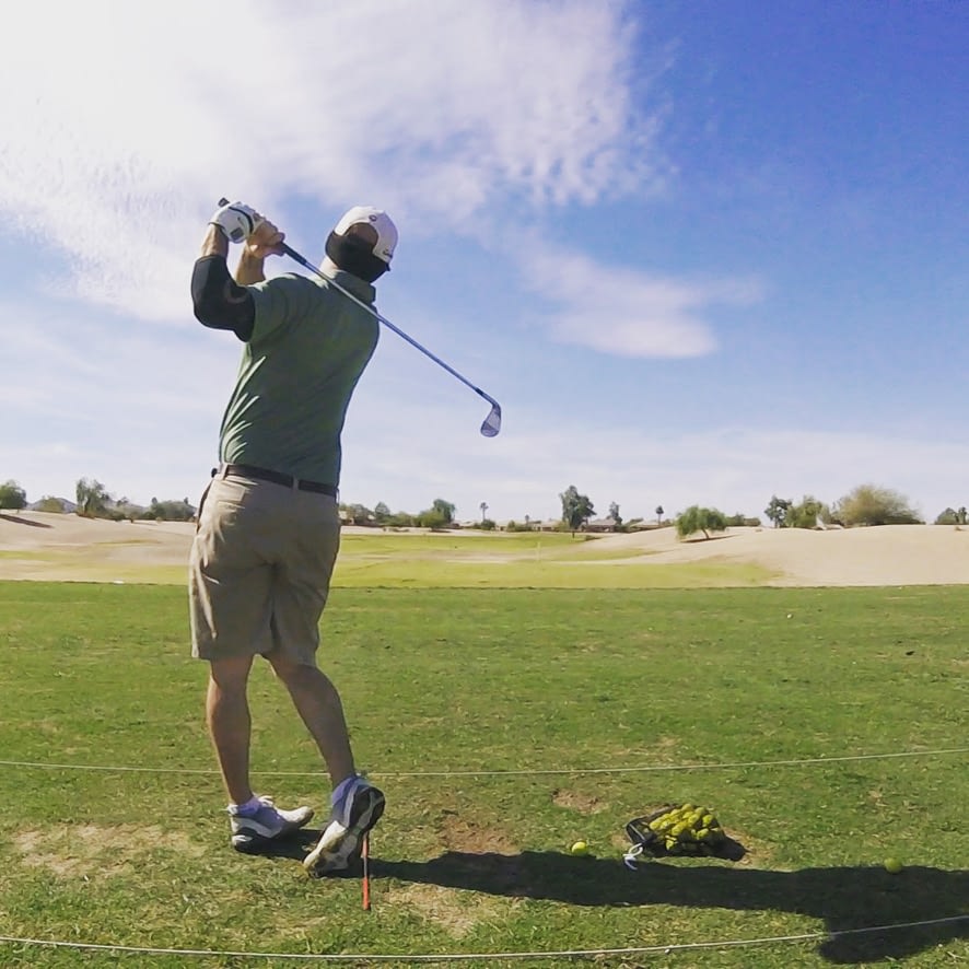 A golfer taking their first swing of the day on a practice green, with the ball mid-air and a clear target in sight. The golfer looks focused and determined, surrounded by vibrant green grass and morning light