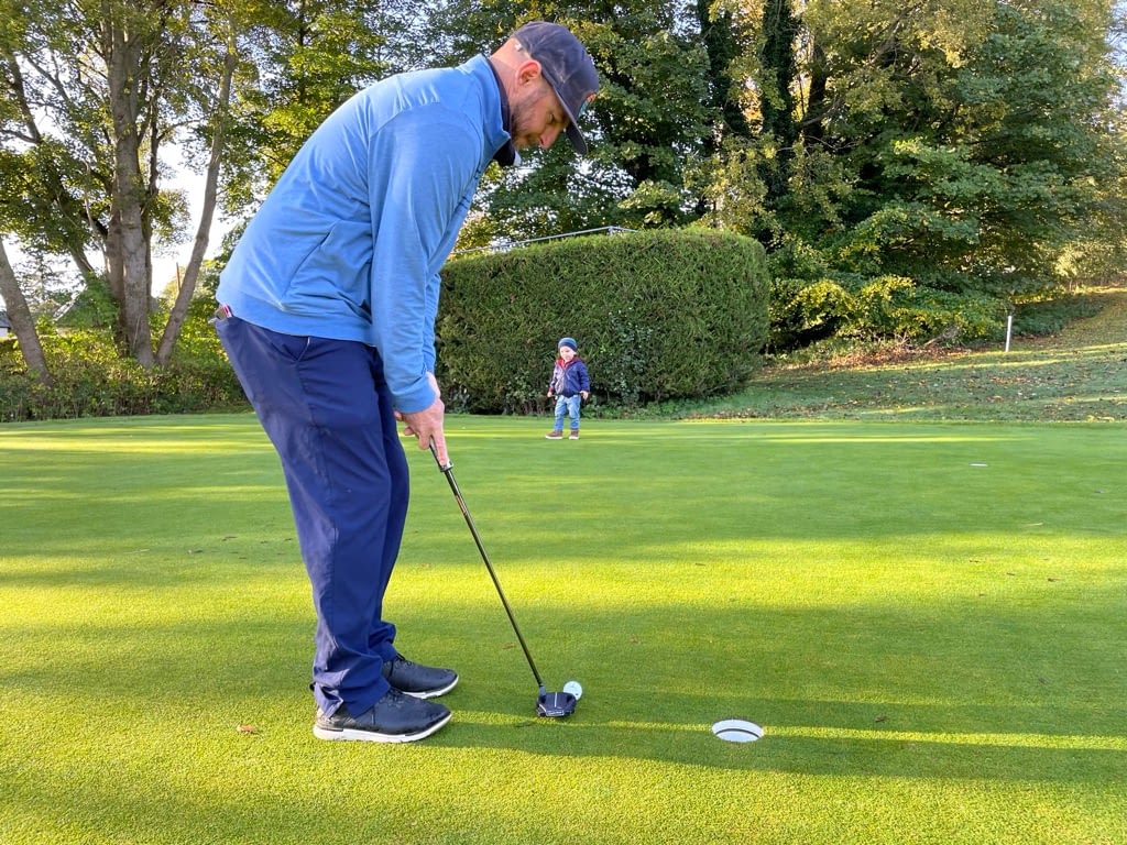 Father working on Putting drills with son watching on practice green