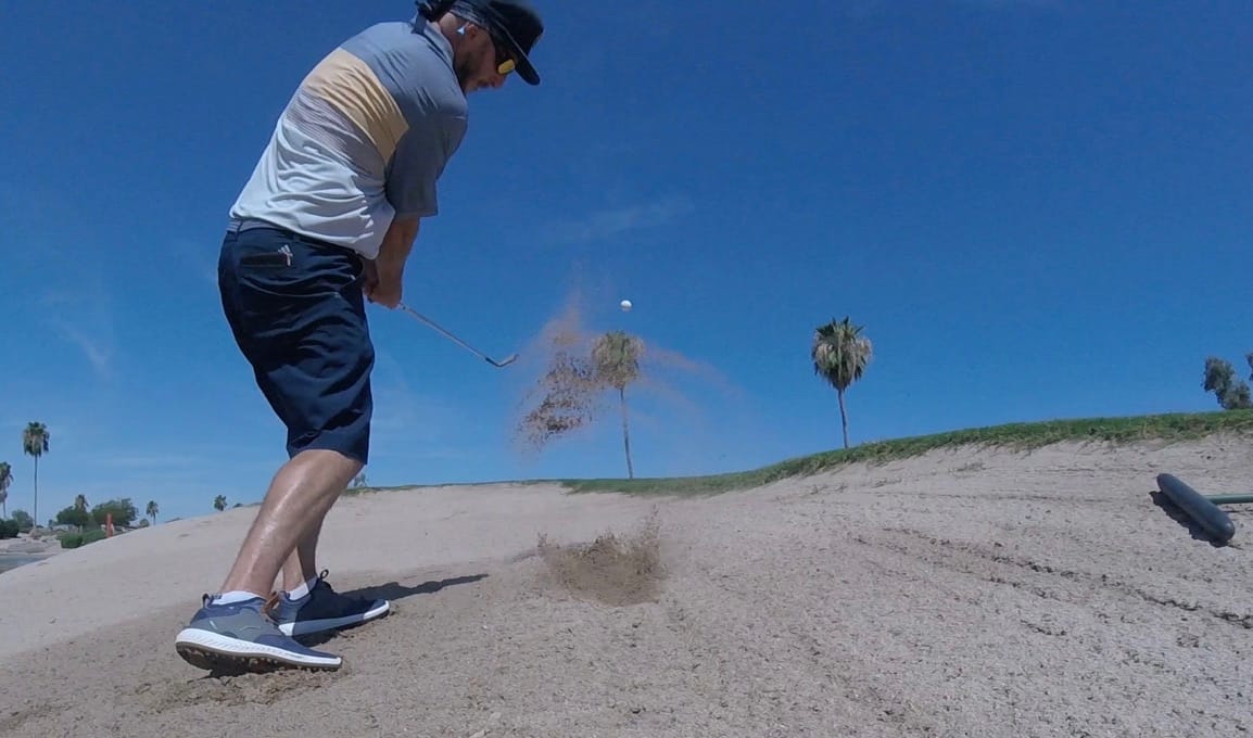 Golfer using wisdom to explode sand out of bunker on golf course